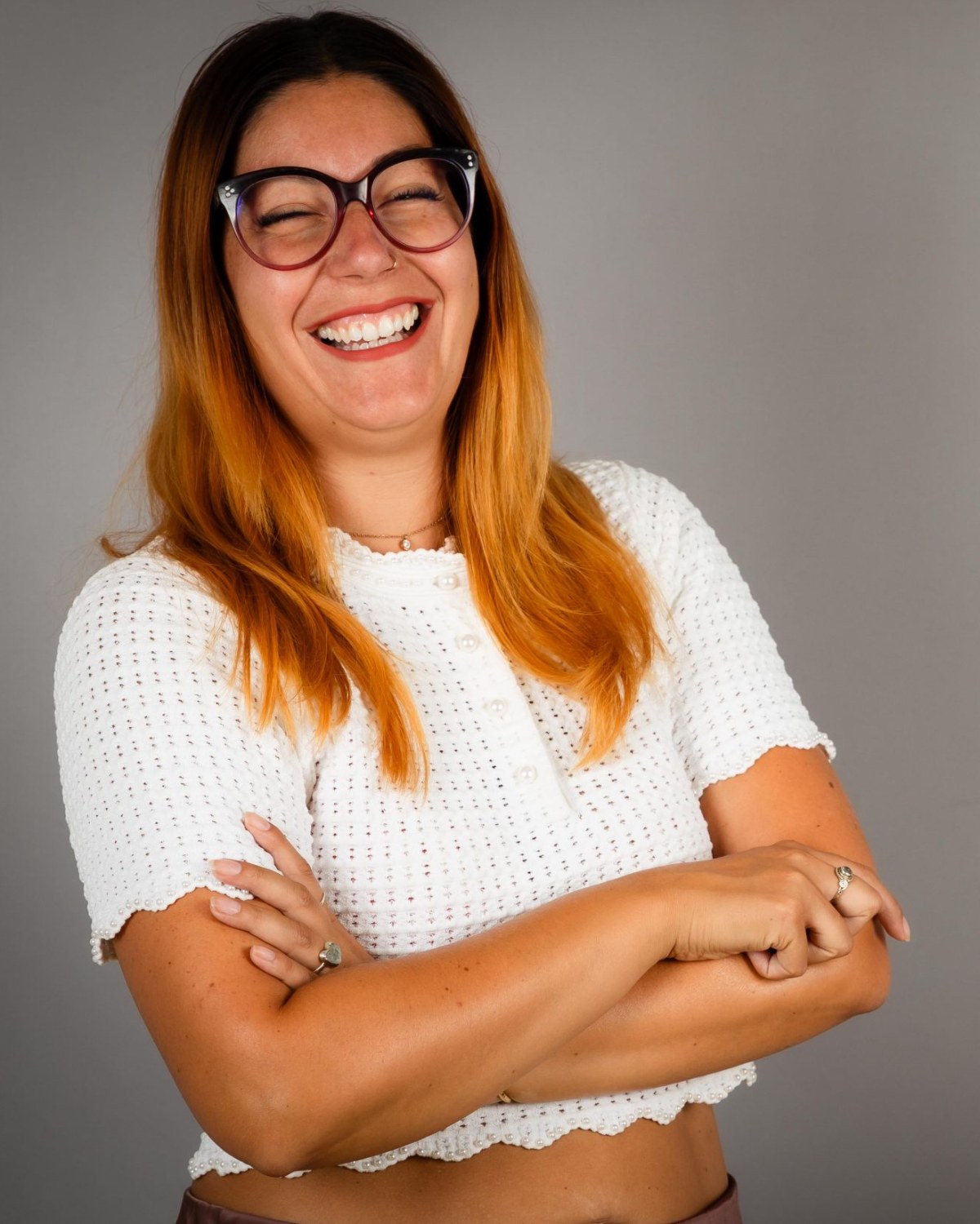 Sandra Steinkönig lacht, die Arme verschränkt, vor grauem Studiohintergrund